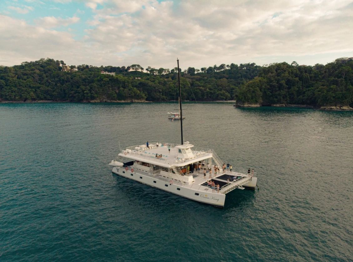 Catamarán blanco en aguas tranquilas con personas a bordo.