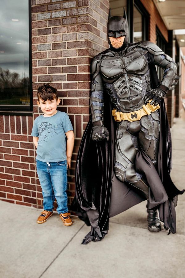 Batman leaning against brick wall with smiling boy. 