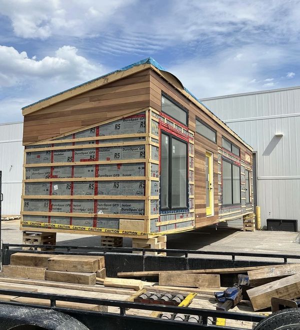 A modern tiny house under construction with wooden siding and large windows.