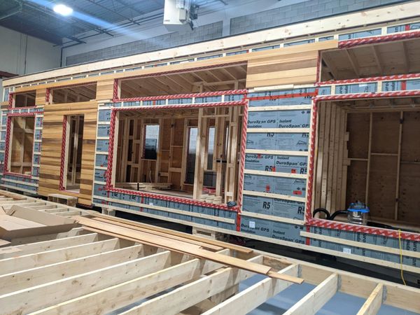 Partially constructed wooden building frame inside a warehouse.