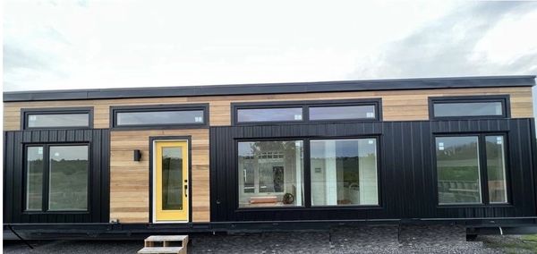 Modern tiny house with wooden and black exterior, yellow door, and large windows.