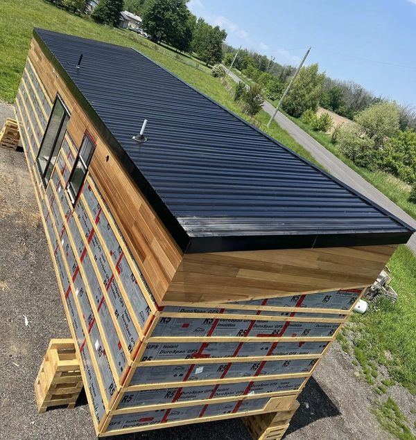 A modern tiny house under construction with wood siding and black metal roof.
