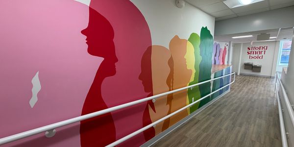 Colorful silhouette mural of diverse faces along a hallway with inspirational words ahead.