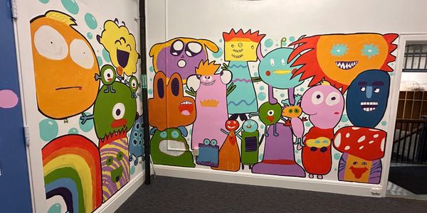 Colorful cartoon monster mural on two adjacent walls in a room.