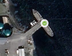 A large ship docked at a pier near industrial buildings beside the ocean.