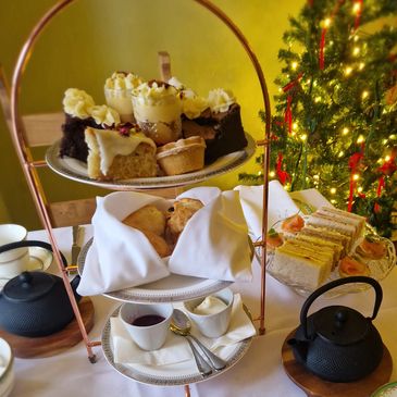 Afternoon tea set with desserts and tea pots by a Christmas tree.