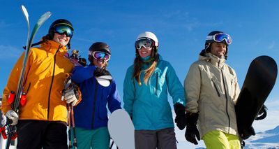 Group of friends holding skis and a snowboard