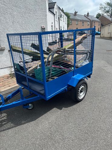 Blue utility trailer loaded with scrap wood and metal on a residential street.