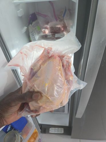Hand holding vacuum-sealed raw chicken in front of an open freezer.