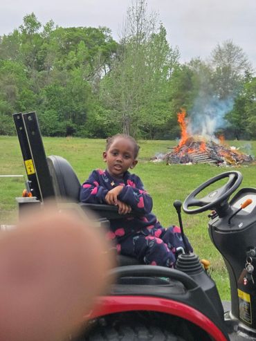Child sitting on a tractor with a large bonfire in the background.