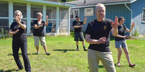 Group of 5 people practice Tai Chi in a back yard.