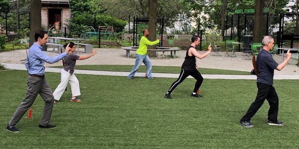 A group of 5 people practice Tai Chi in a park.