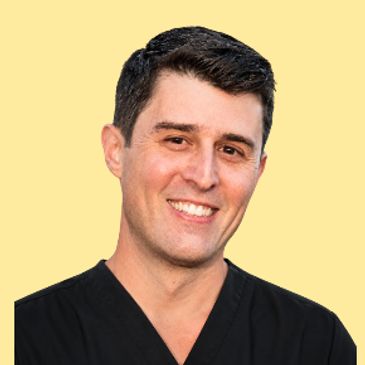 Smiling man in black medical scrubs against a yellow background.
