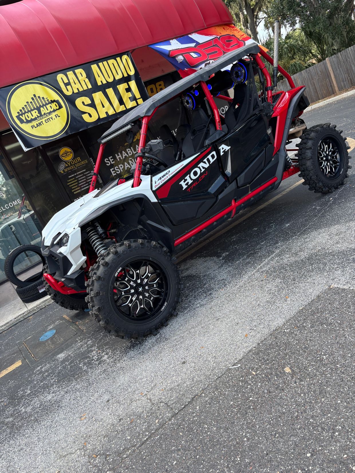 Red and white Honda Talon off-road vehicle parked outside a car audio store.