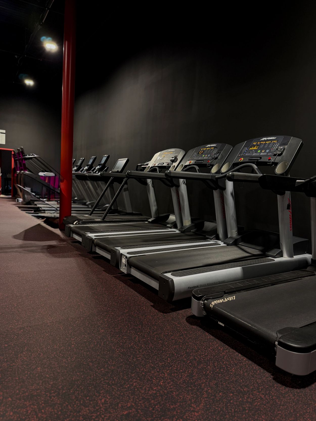 Row of treadmills in a dimly lit gym.