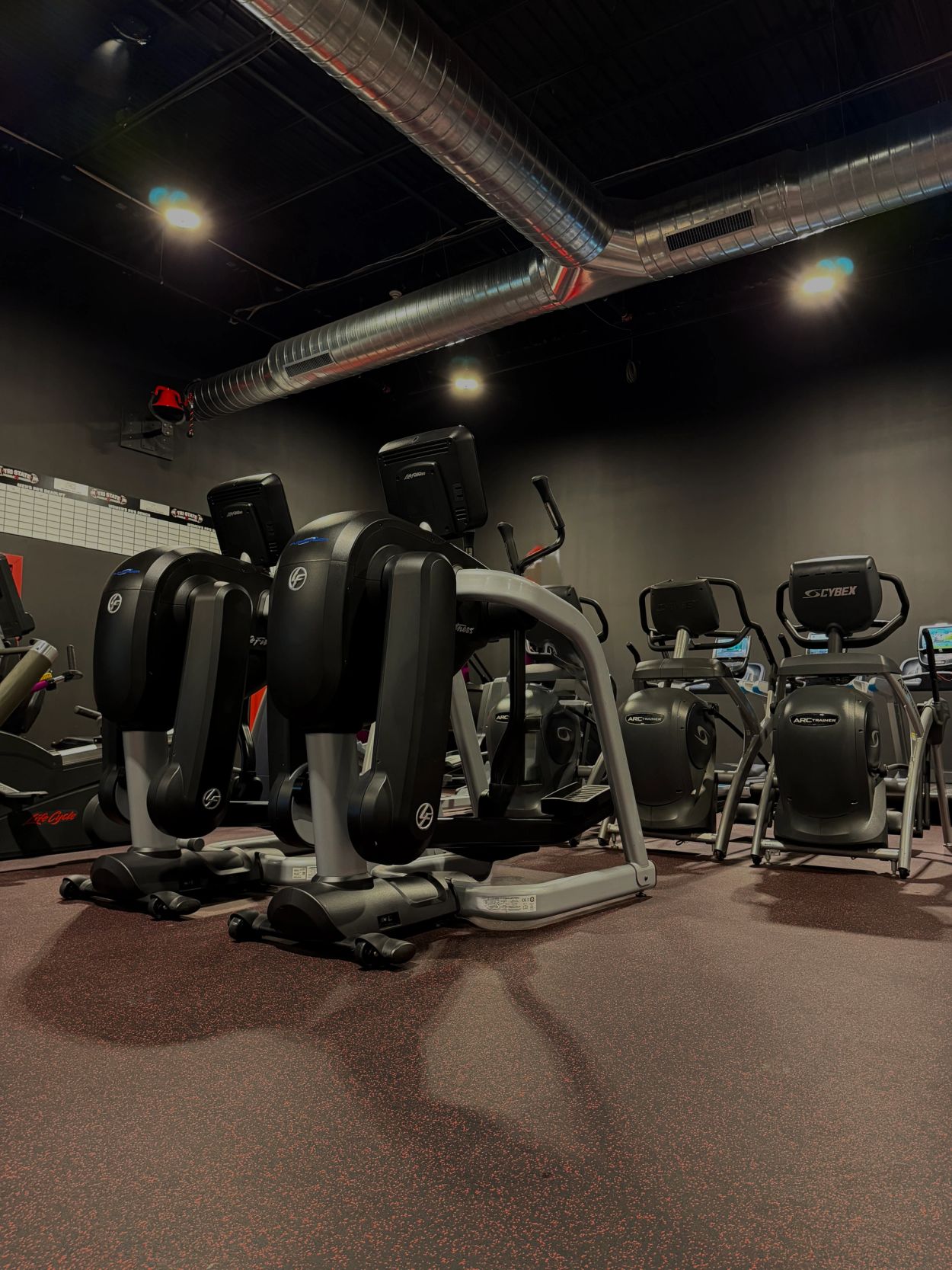 Gym with cardio exercise machines under industrial lighting.