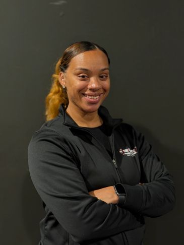 Smiling woman with crossed arms against a dark background.
