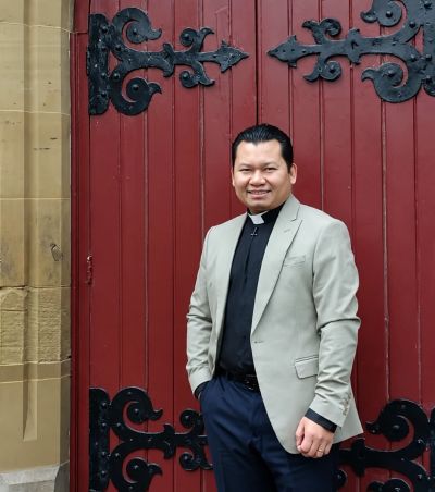 Man in clerical attire stands by ornate red door.