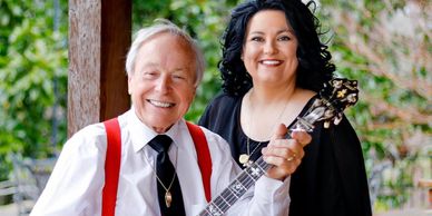 Elderly man with a banjo and smiling woman posing outdoors.
