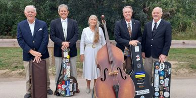 A group of five people posing with musical instrument cases outdoors.