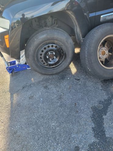 A car with a removed wheel and a spare tire mounted on a black steel rim.