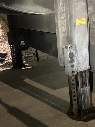 Close-up of a metal support leg with adjustment holes on concrete ground.