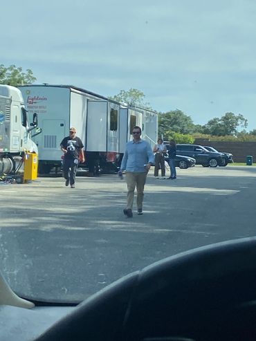 People walking near trailers and parked cars on a sunny day.