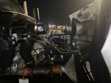 Close-up of a truck engine at night with visible pipes and hoses.