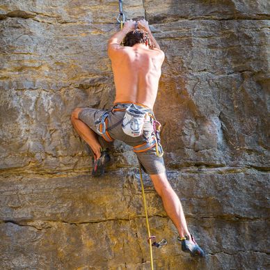 a male-presenting body climbs a rock wall on belay