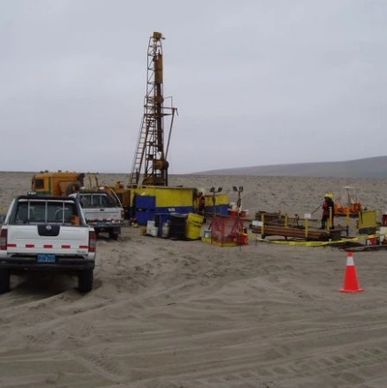 Drilling operation with trucks and equipment in a barren desert landscape.
