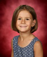 young girl with short hair smiling and posing for school portrait against pink background