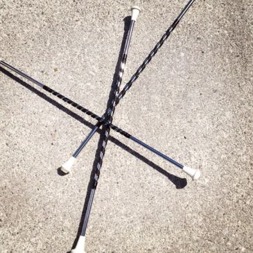 Four black and silver knitting needles arranged in a crisscross pattern on concrete.