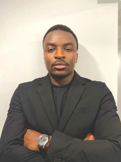 Confident man in a black blazer with arms crossed and a wristwatch.