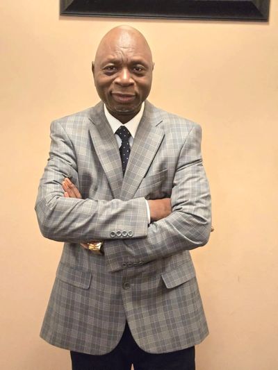 Man in a gray plaid suit with arms crossed, smiling.