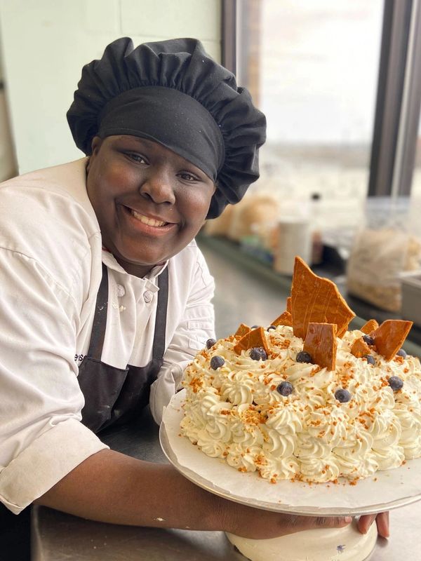 Smiling chef holding a decorated cake.