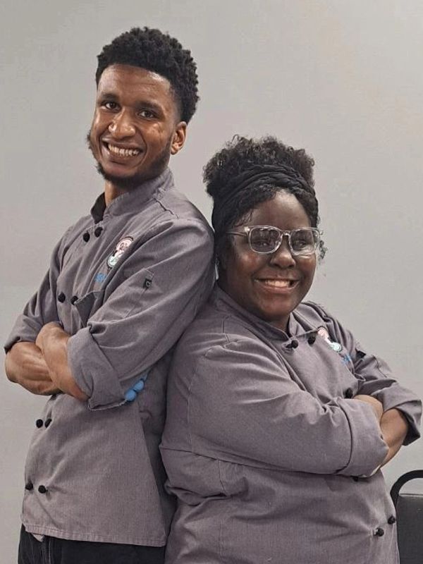 Two chefs smiling back-to-back in gray uniforms.