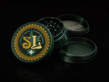 Dark green herb grinder with a decorative lid and a scraper tool.
