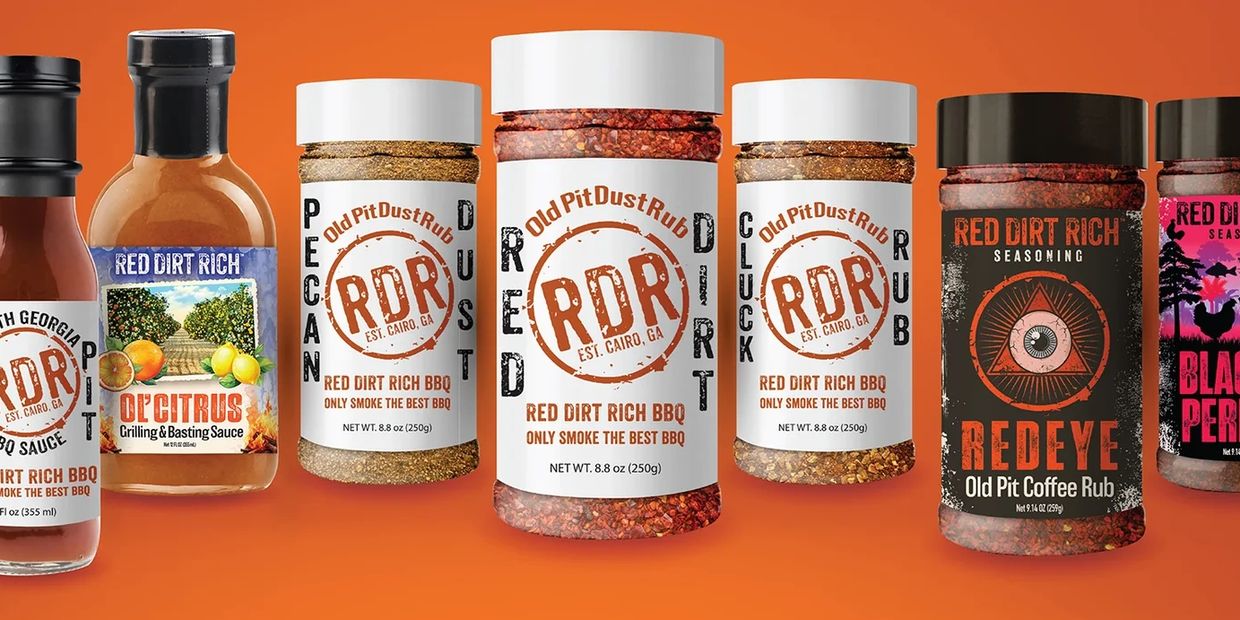 Lineup of Red Dirt Rich BBQ sauces and rubs on an orange background.