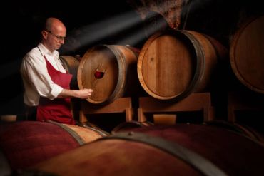 Man inspecting wine in a cellar with barrels.