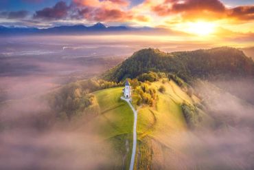 A church on a hill during sunset with fog and mountains.