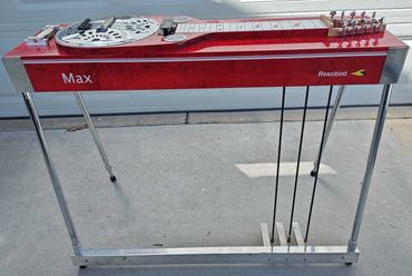A red Resobird Max pedal steel guitar with chrome legs and three foot pedals.