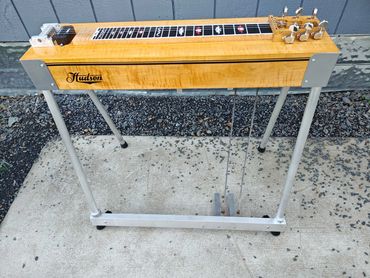 A wooden Hudson lap steel guitar with metal legs on a concrete surface.