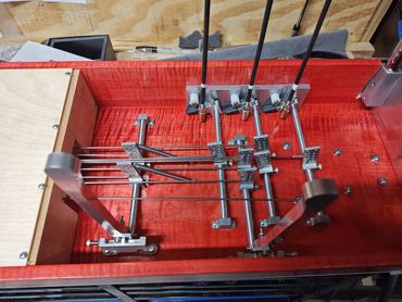 Mechanical assembly with metal rods and levers on a red wooden base.
