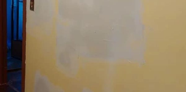 A yellow wall with several light gray patches and a wooden floor.