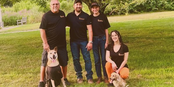Group of four people with two dogs posing outdoors on grass.
