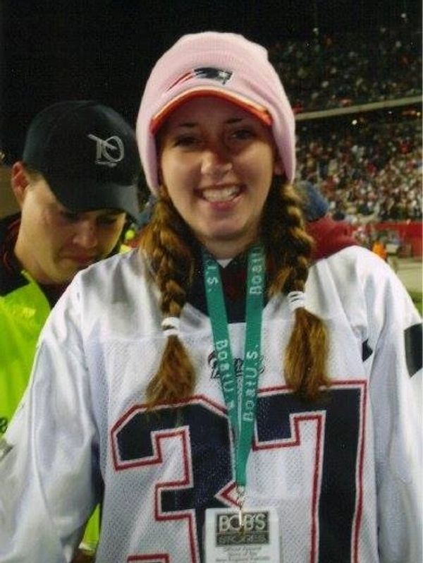 Becky in a New England Patriots jersey and pink hat at a crowded stadium.