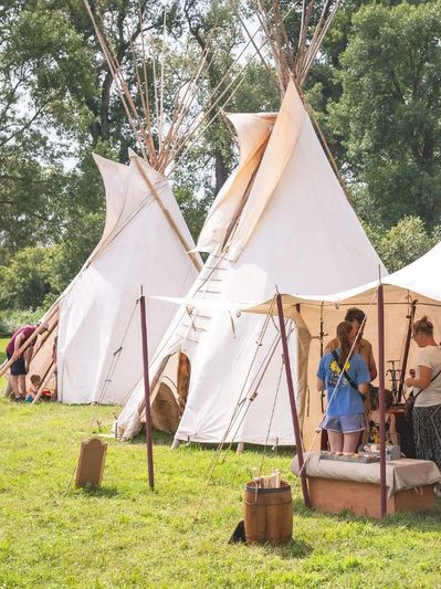 Traditional teepees set up in a grassy area with people gathered nearby.