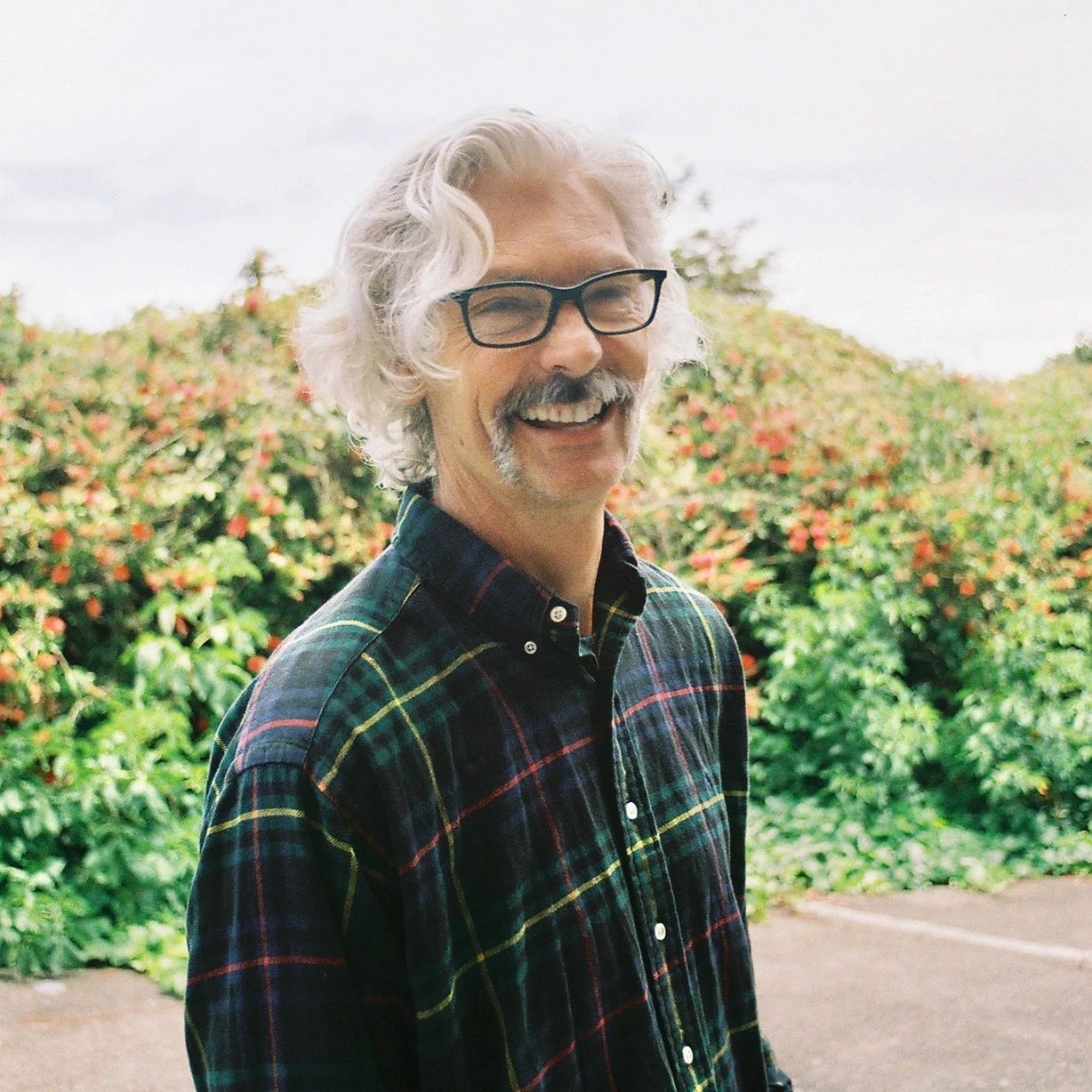 Smiling man with gray hair and mustache outdoors.