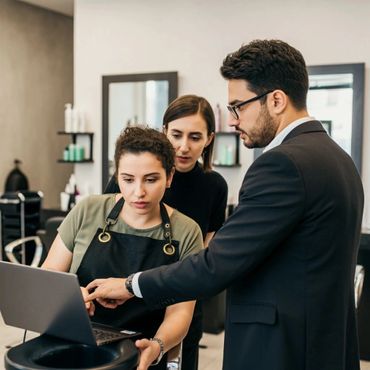 Three professionals discussing work on a laptop in a salon setting.