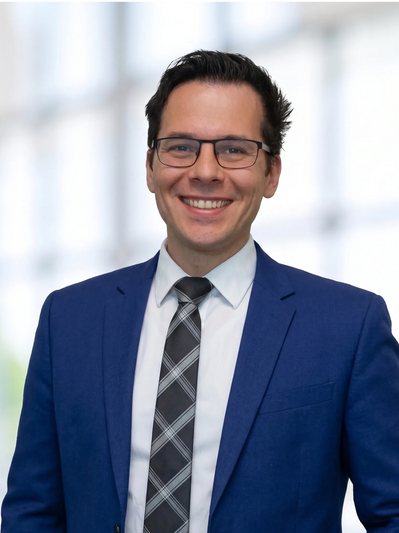 Smiling young man in a blue suit and glasses posing confidently.